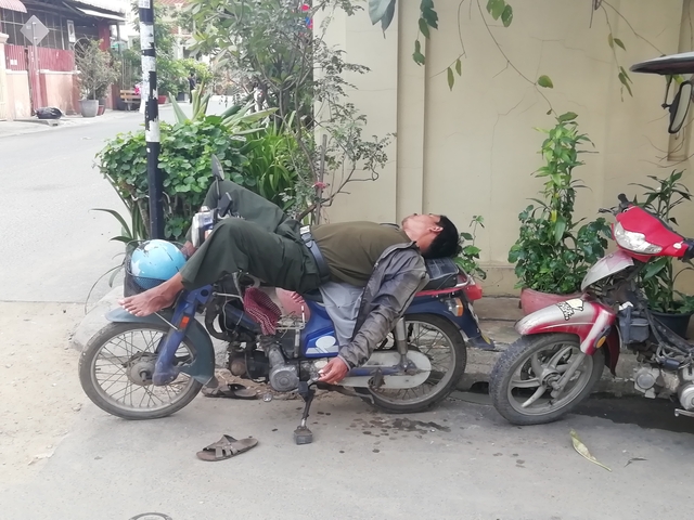 Person resting on a motorcycle by the roadside.