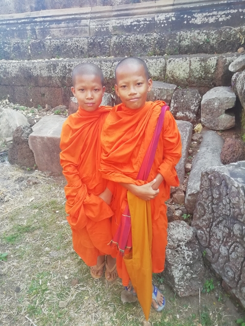 Two young monks in orange robes standing by stone carvings.