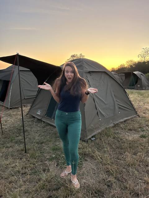 Woman standing in front of a tent with a sunset sky.
