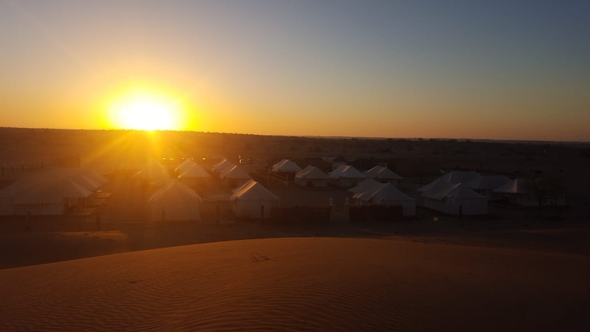 Tents set up in a desert as the sun sets on the horizon.