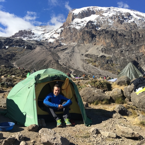 Person sitting in front of a tent with a mountain backdrop.