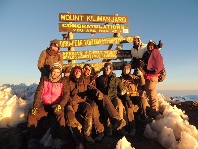 Group of people at Uhuru Peak with a congratulatory sign.