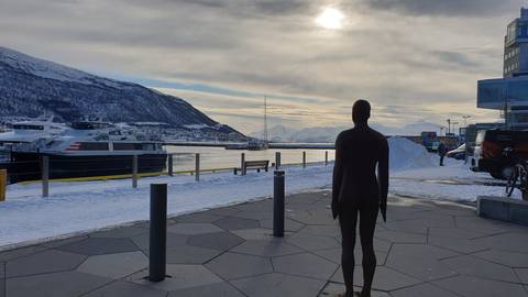 Sculpture of a person overlooking a snowy harbor.