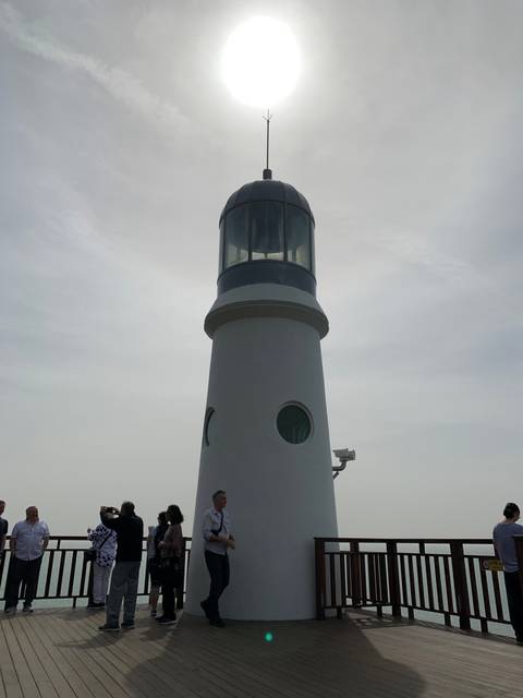 Lighthouse viewed against the sun with visitors nearby.