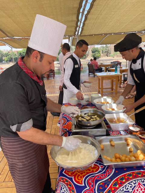 Chefs preparing food on an outdoor table under a canopy.