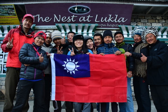 Group posing with a flag in front of a lodge in Lukla.