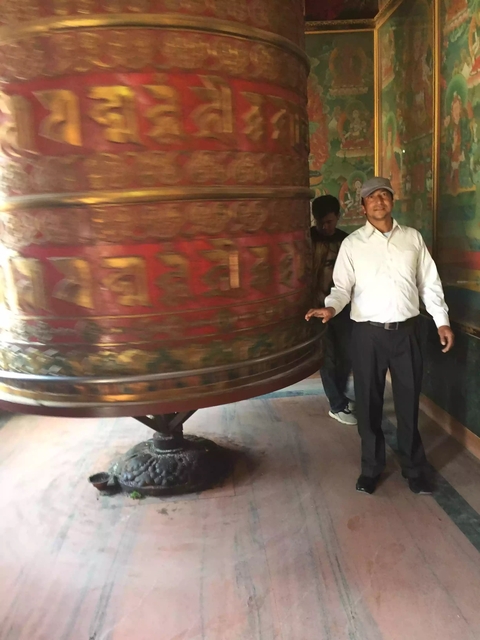 Man posing with a large revolving prayer wheel.