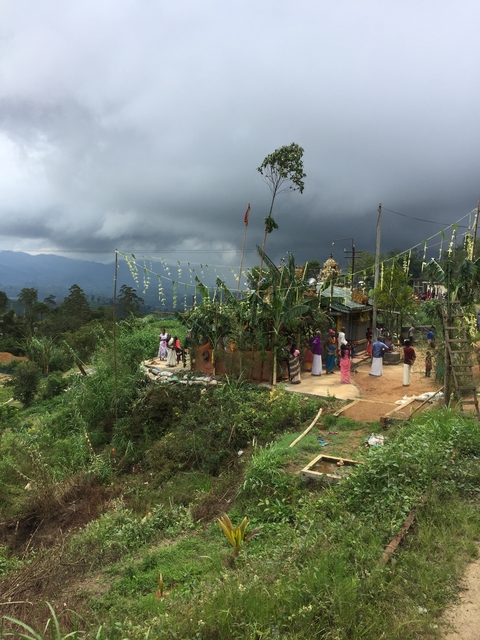 A cultural gathering with people around a decorated area with cloudy skies.