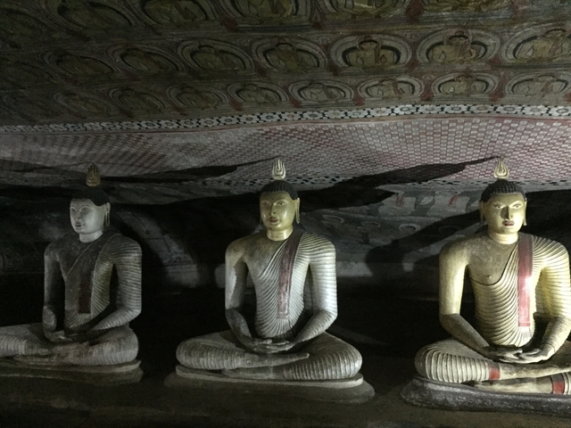 Three seated Buddha statues inside a cave.