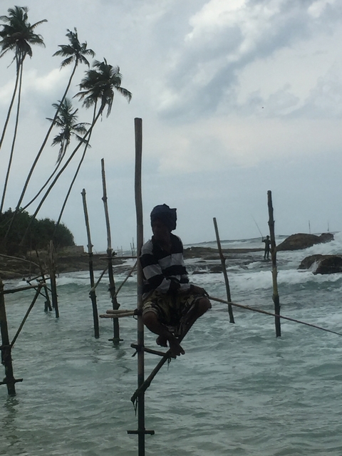 Stilt fisherman silhouetted against a cloudy seaside setting.