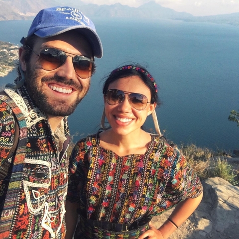 Two people in colorful clothing smiling with a scenic lake background.