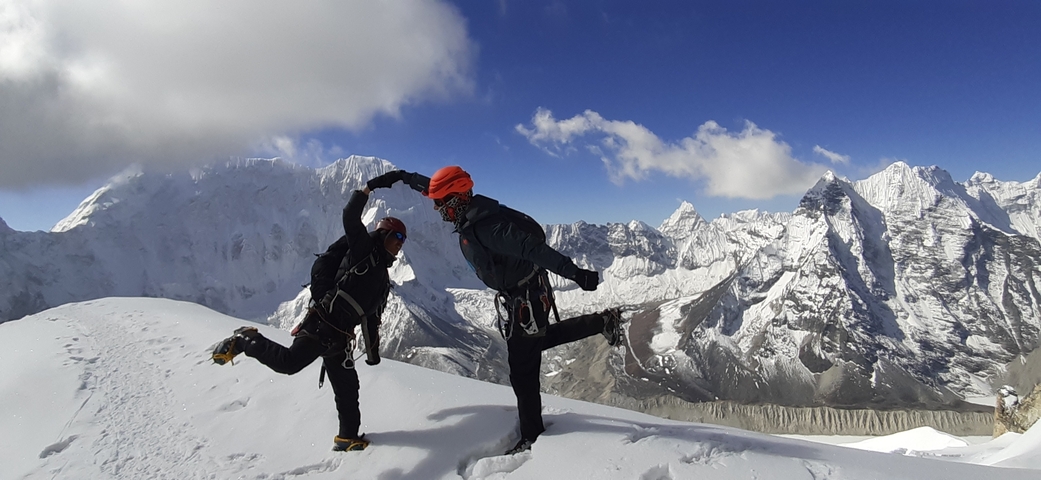 Two climbers striking playful poses on a snowy mountain peak.