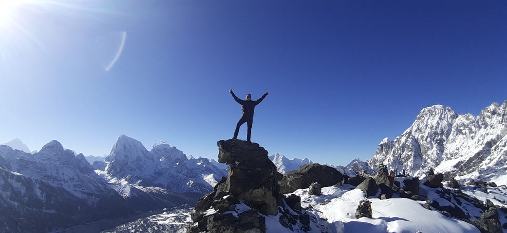 A climber celebrating on top of a rocky peak surrounded by snowy mountains.