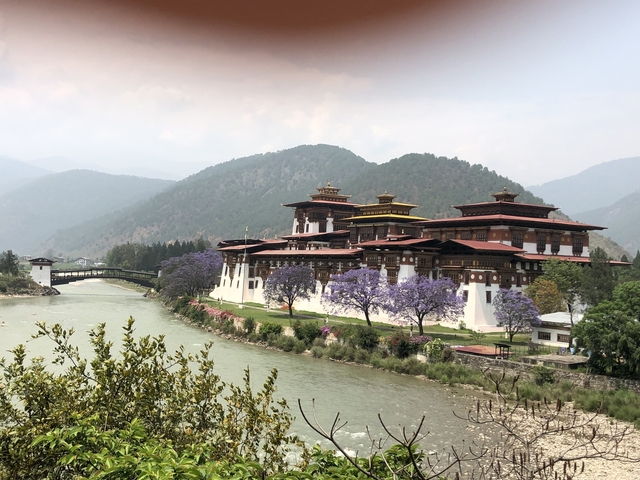 Scenic view of a river and a traditional Bhutanese fortress with mountains.