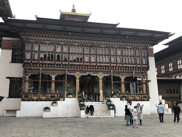 People at the entrance of a traditional Bhutanese building with intricate designs.