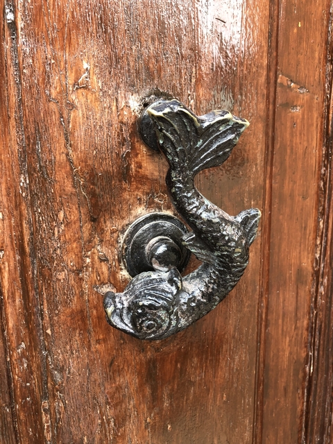 Close-up of an ornate door knocker featuring a mermaid design on a wooden door.