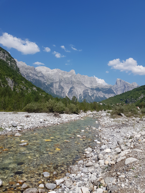 A clear mountain stream with rocky banks and a mountain range.