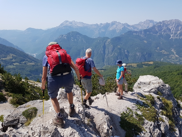 Hikers with backpacks on a rocky peak overlooking mountains.