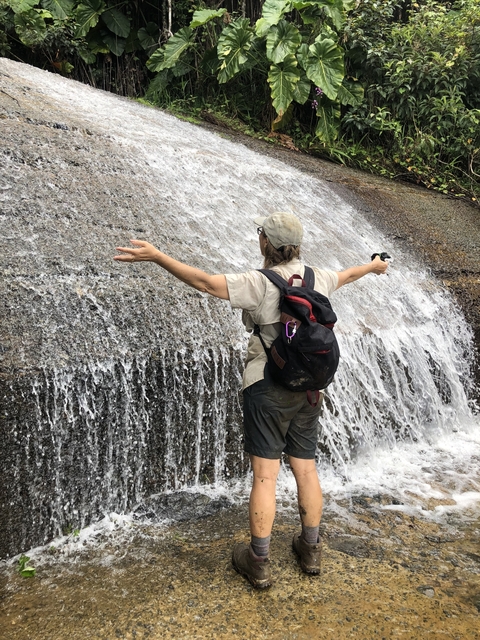 Person enjoying a waterfall with arms outstretched.