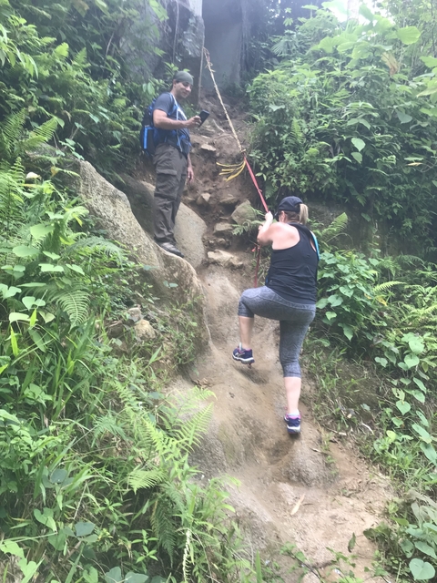 Hiker climbing up a rocky path with a rope.