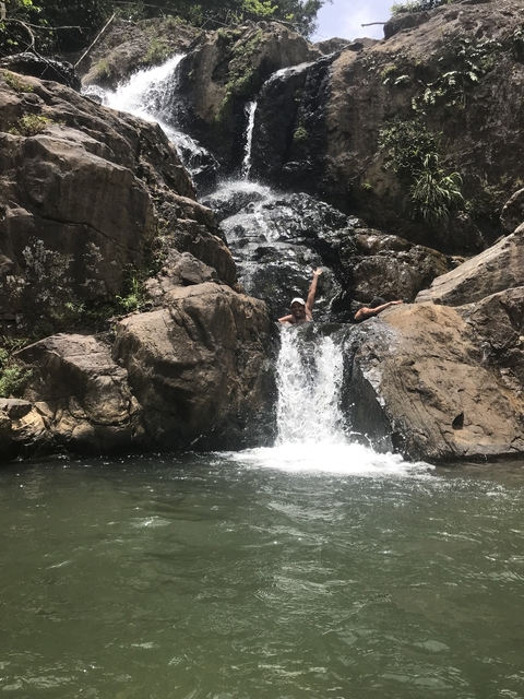 Two people enjoying a small waterfall surrounded by large rocks.