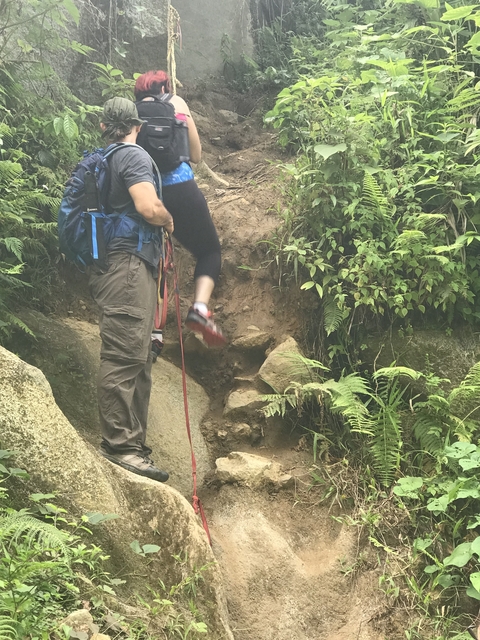 Person hiking up a rocky trail with a rope.