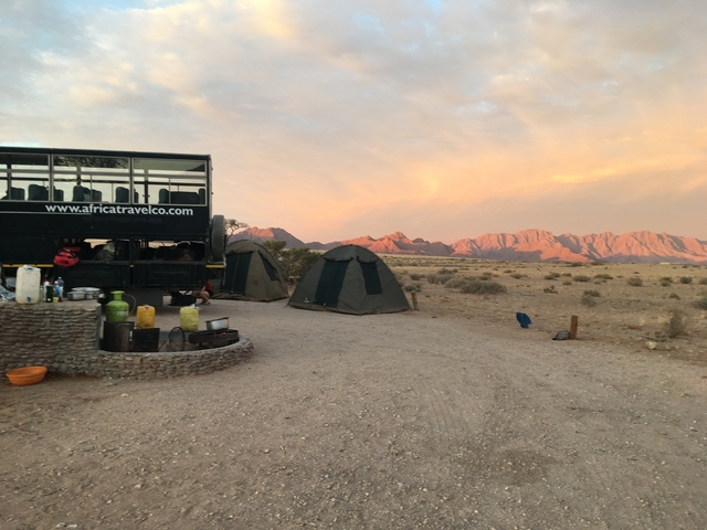 A campsite with tents and a safari vehicle at sunset in a desert landscape.