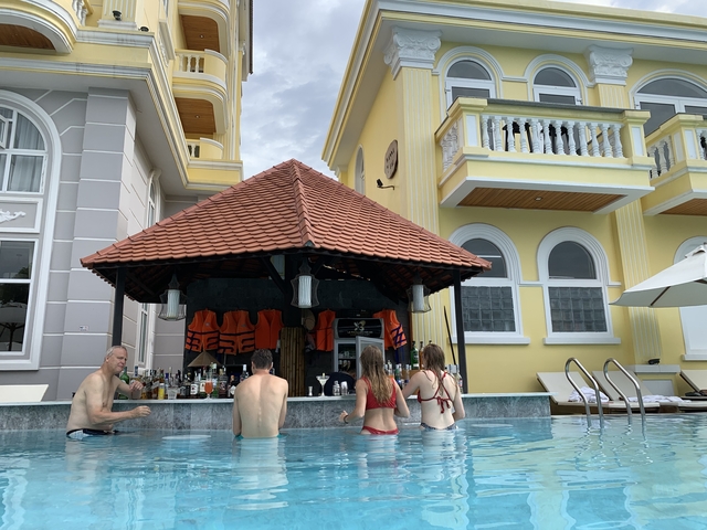 People enjoying a swim-up bar in a pool with colorful buildings in the background.
