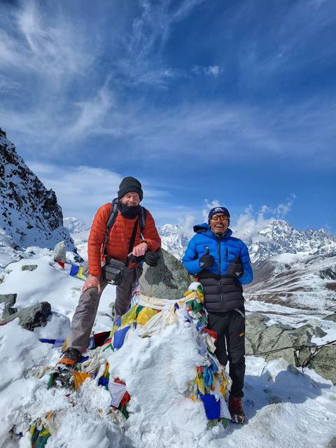 Two people with colorful flags against a snowy mountain backdrop.