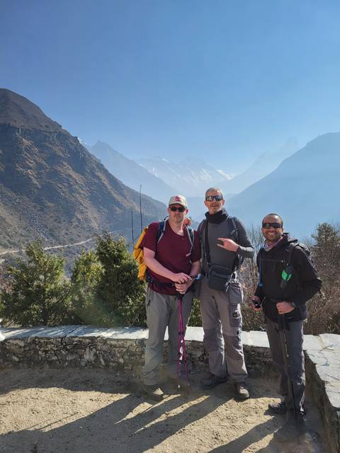 Three people standing with trekking poles on a mountain trail.