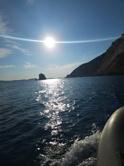 A seascape with the sun setting over the horizon, casting reflections on the water.