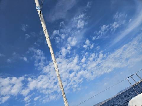 A sailing mast against a blue sky filled with clouds.
