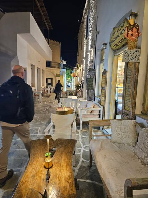 A nighttime street scene with tables and chairs at a cafe.