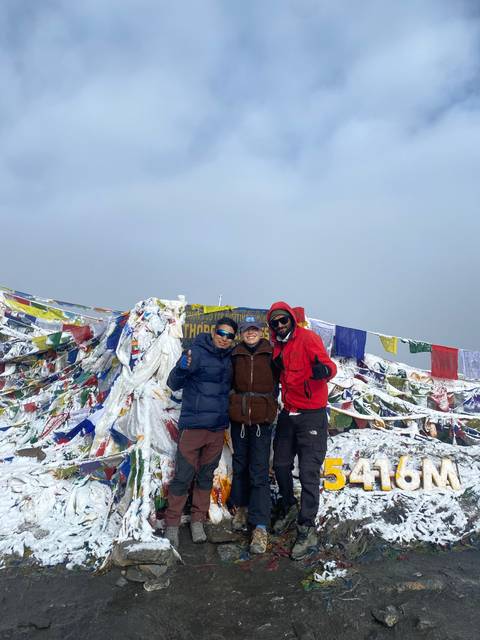 Three hikers standing next to a sign at a high-altitude pass.
