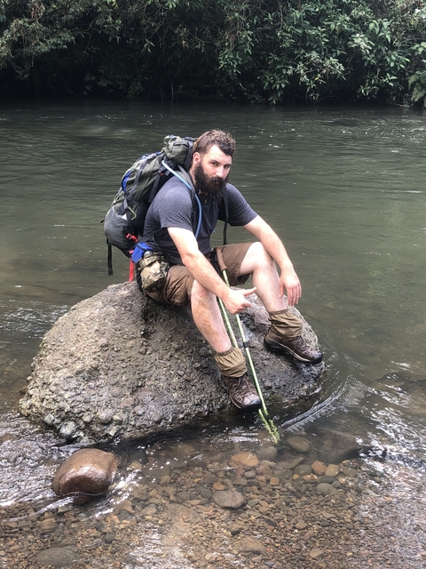 Man resting on a rock by a river.
