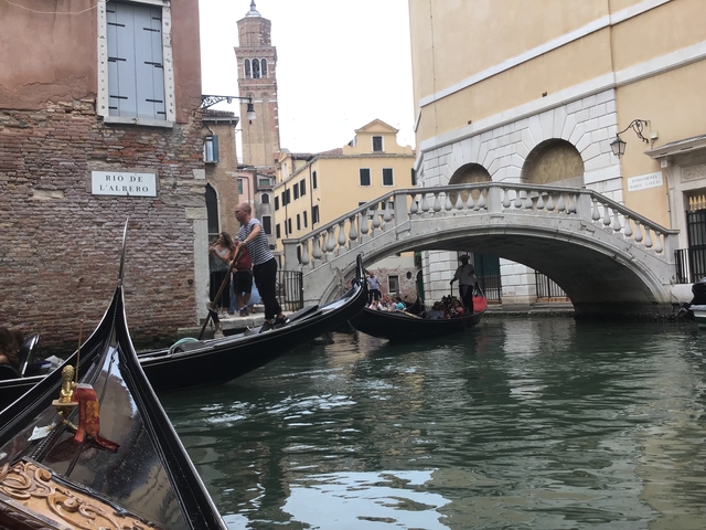 Gondolas navigating a canal in Venice under a bridge.