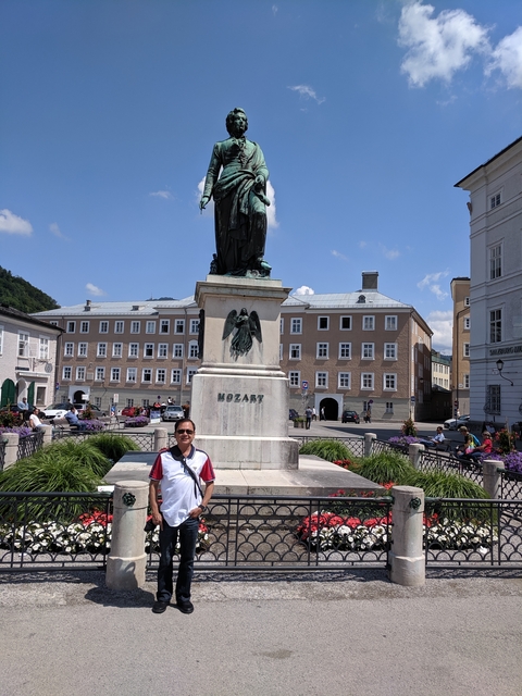 Man in front of a tall statue in a square.
