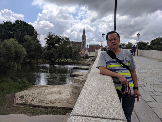 Man on a bridge with a river and church in the background.