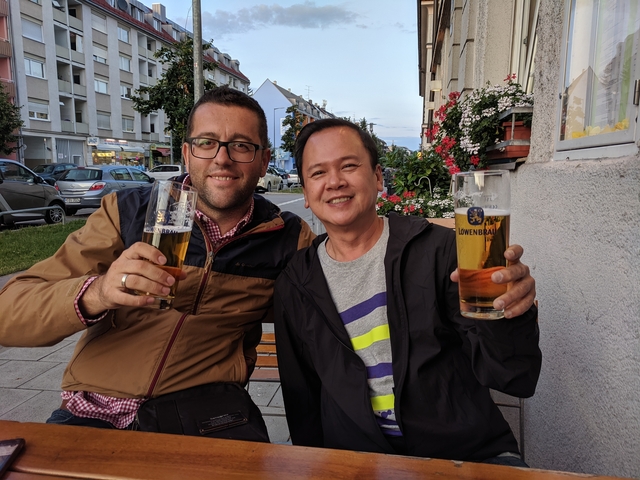 Two men holding beer in an urban setting.