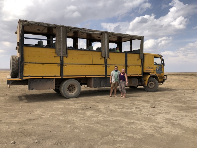 Two people standing in front of a large yellow safari truck.