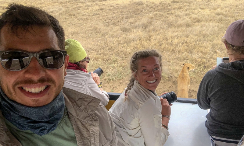 Tourists taking photos of a lion in a safari vehicle.