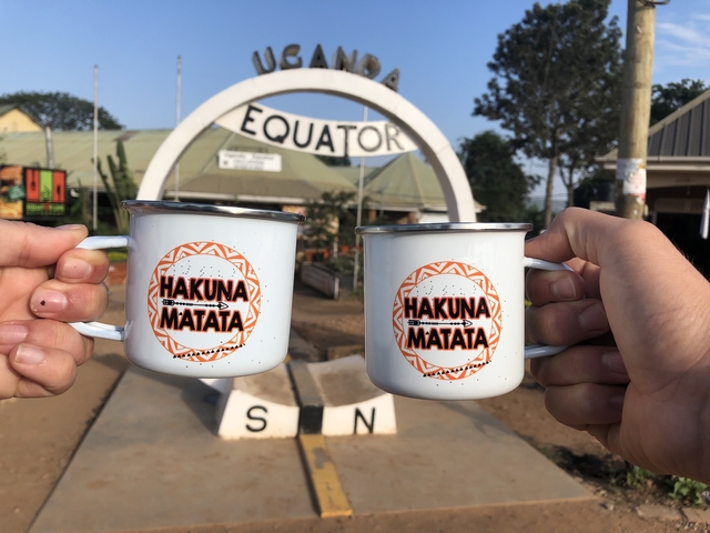 Two mugs with text held in front of an equator monument.