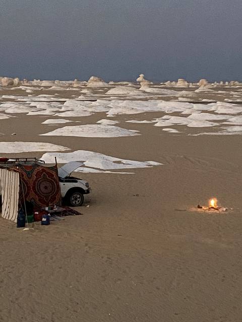 A car and tent in a desert landscape with unique rock formations.