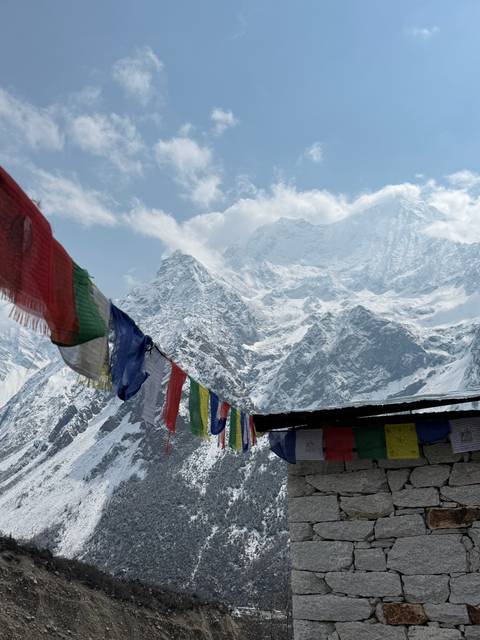 Mountain view with colorful prayer flags and a stone structure.
