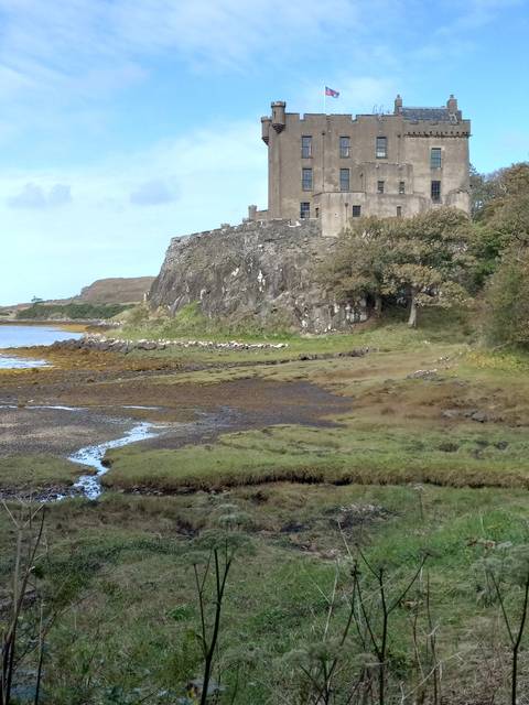 Historic castle with a flag on top overlooking a grassy field.