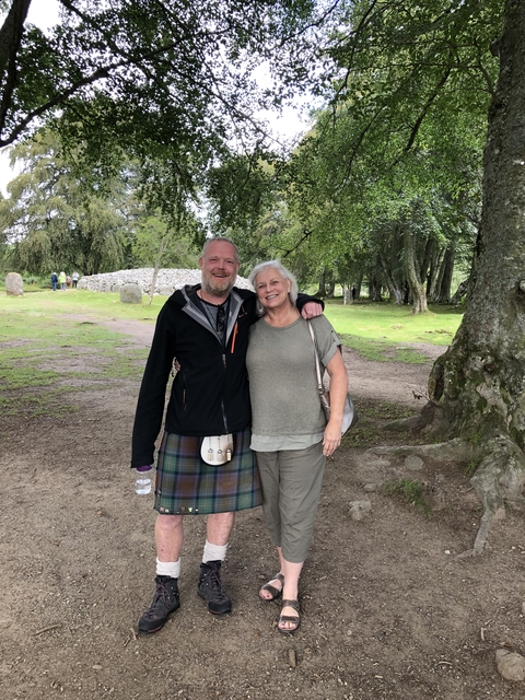 Two people posing outdoors near stone circle.