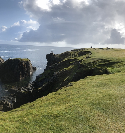 Rugged cliff landscape with grassy edges and two people standing atop