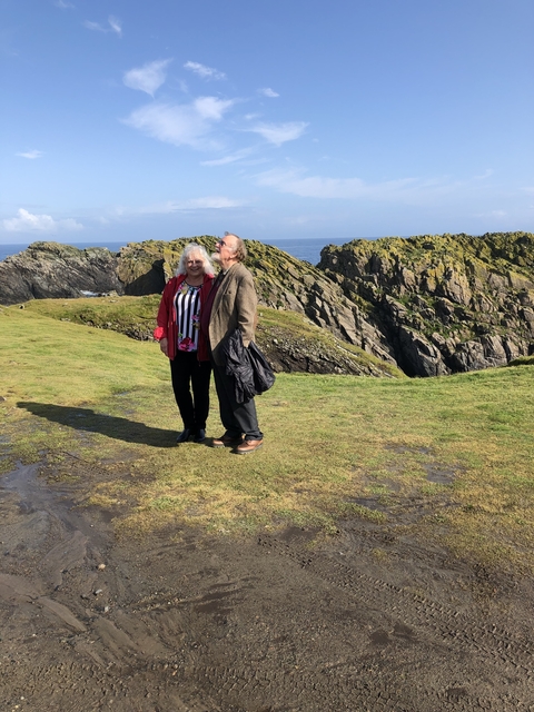 Couple standing on green cliffs with ocean behind.