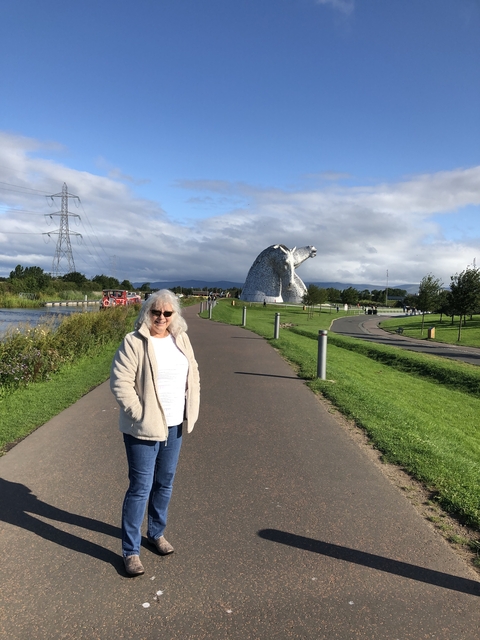 Elderly woman walking along a canal path with a large sculpture in the background