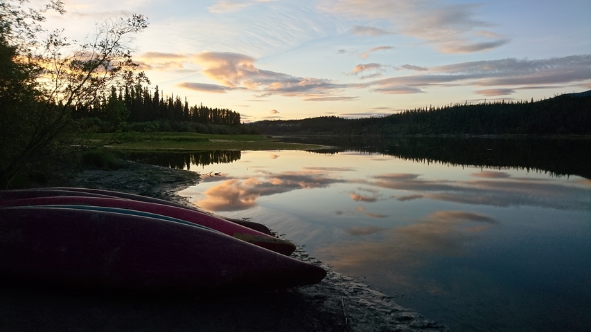 Canoes on the river bank at sunset with vibrant reflections.